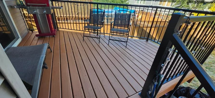 Deck after restoration: freshly stained warm brown boards behind a black metal railing