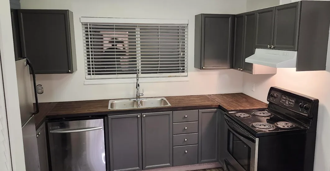 Kitchen after renovation: grey shaker cabinets, butcher-block counters and a new sink under the window